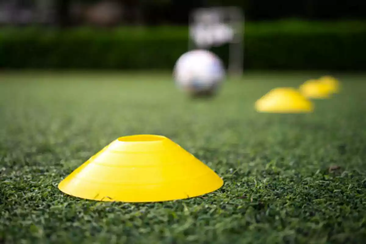 Yellow training cones on grass with a blurred soccer ball in the background Yellow training cones on grass with a blurred soccer ball in the background