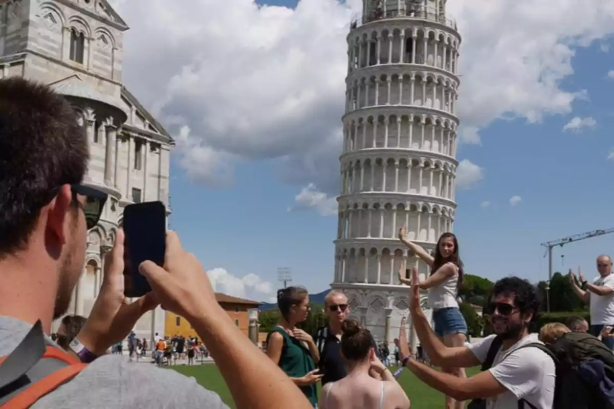 Turistas posan frente a la Torre de Pisa simulando que la sostienen mientras otra persona toma una foto