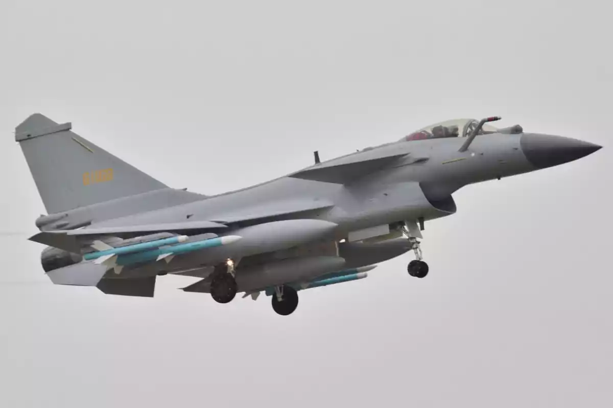 Avión de combate gris volando con el tren de aterrizaje desplegado y misiles bajo las alas en un cielo nublado Avión de combate gris volando con el tren de aterrizaje desplegado y misiles bajo las alas en un cielo nublado