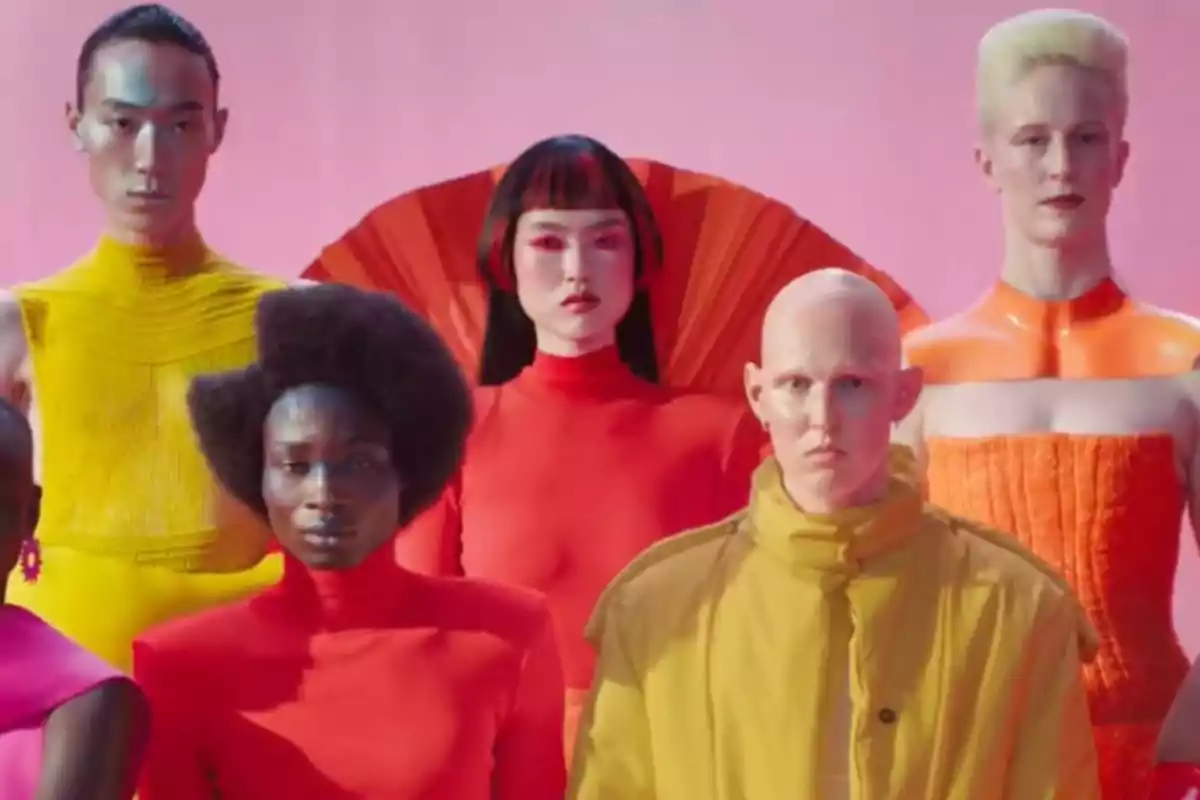 Grupo de personas con diferentes estilos y colores de ropa posando frente a un fondo rosa