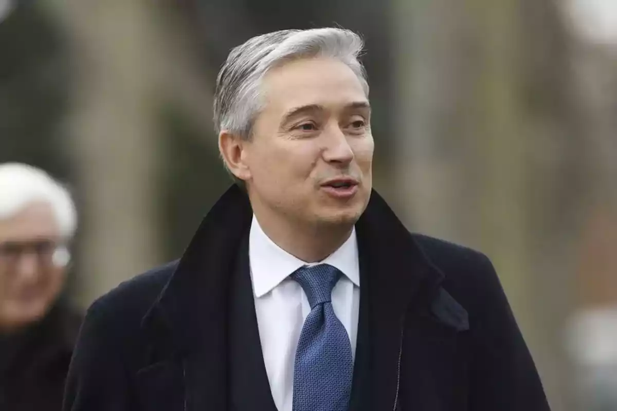 Hombre de cabello canoso con traje y corbata azul hablando al aire libre