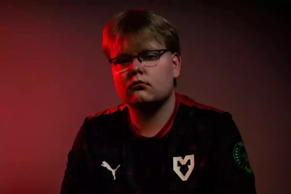 Joven con gafas y camiseta negra con logotipo blanco posando bajo una luz roja Joven con gafas y camiseta negra con logotipo blanco posando bajo una luz roja