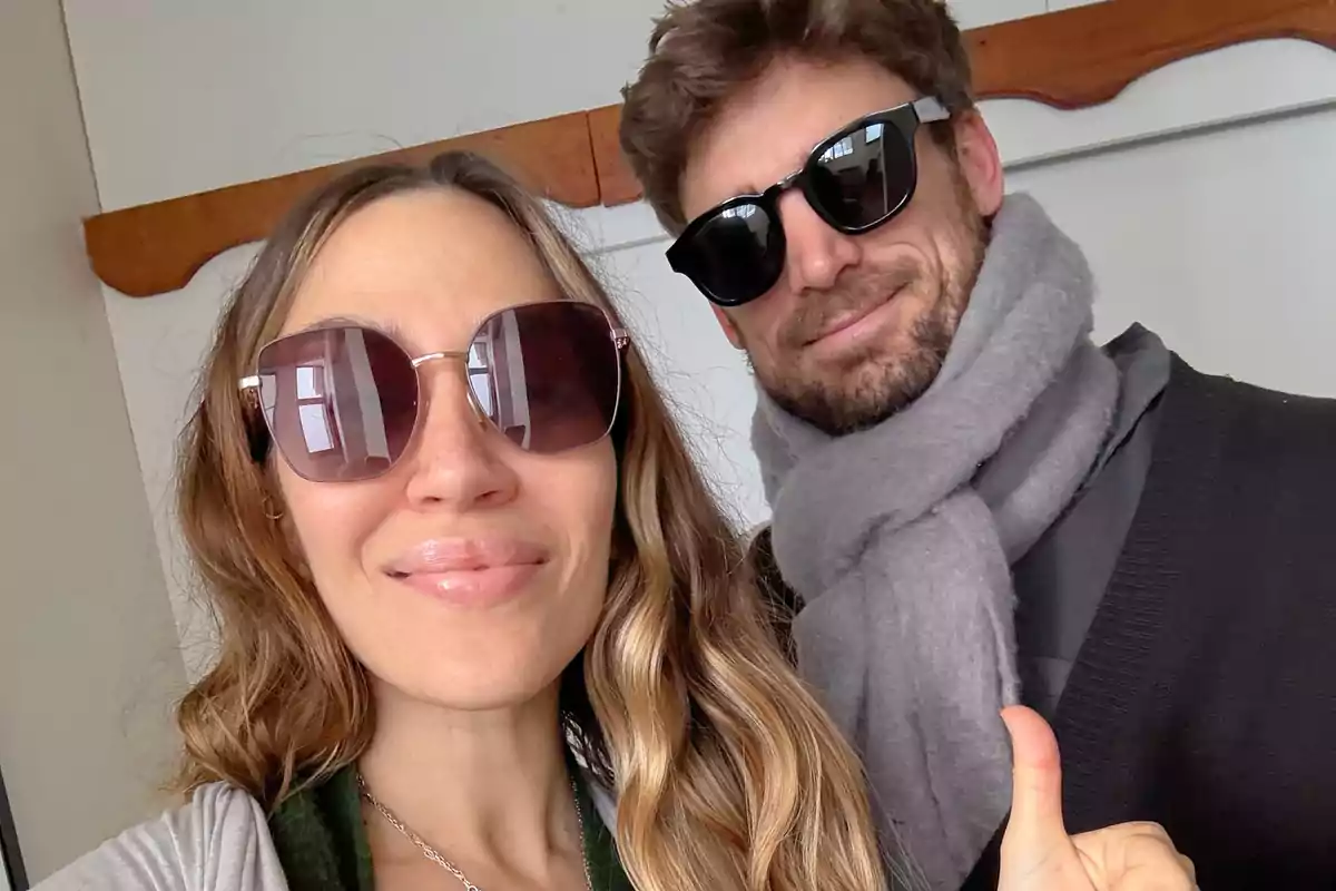 Dos personas sonríen usando gafas de sol, una de ellas lleva bufanda gris y la otra hace un gesto de pulgar arriba Dos personas sonríen usando gafas de sol, una de ellas lleva bufanda gris y la otra hace un gesto de pulgar arriba
