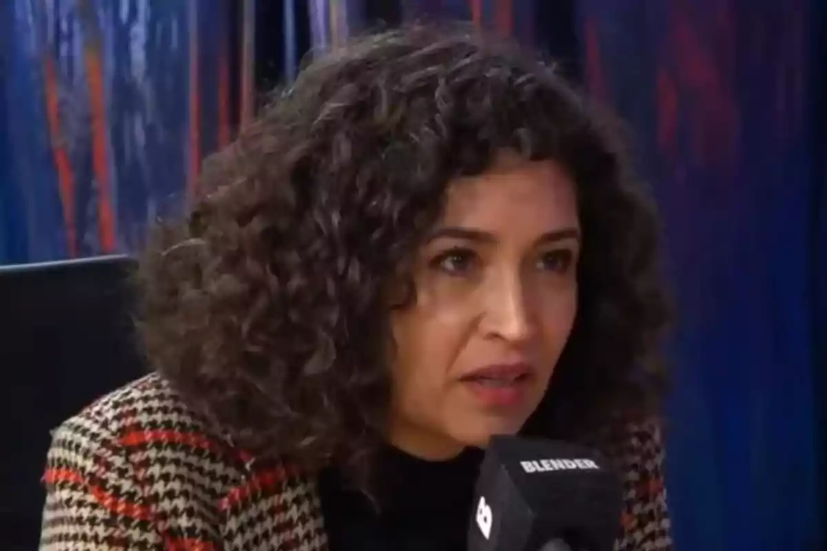 Mujer de cabello rizado hablando frente a un micrófono durante una entrevista
