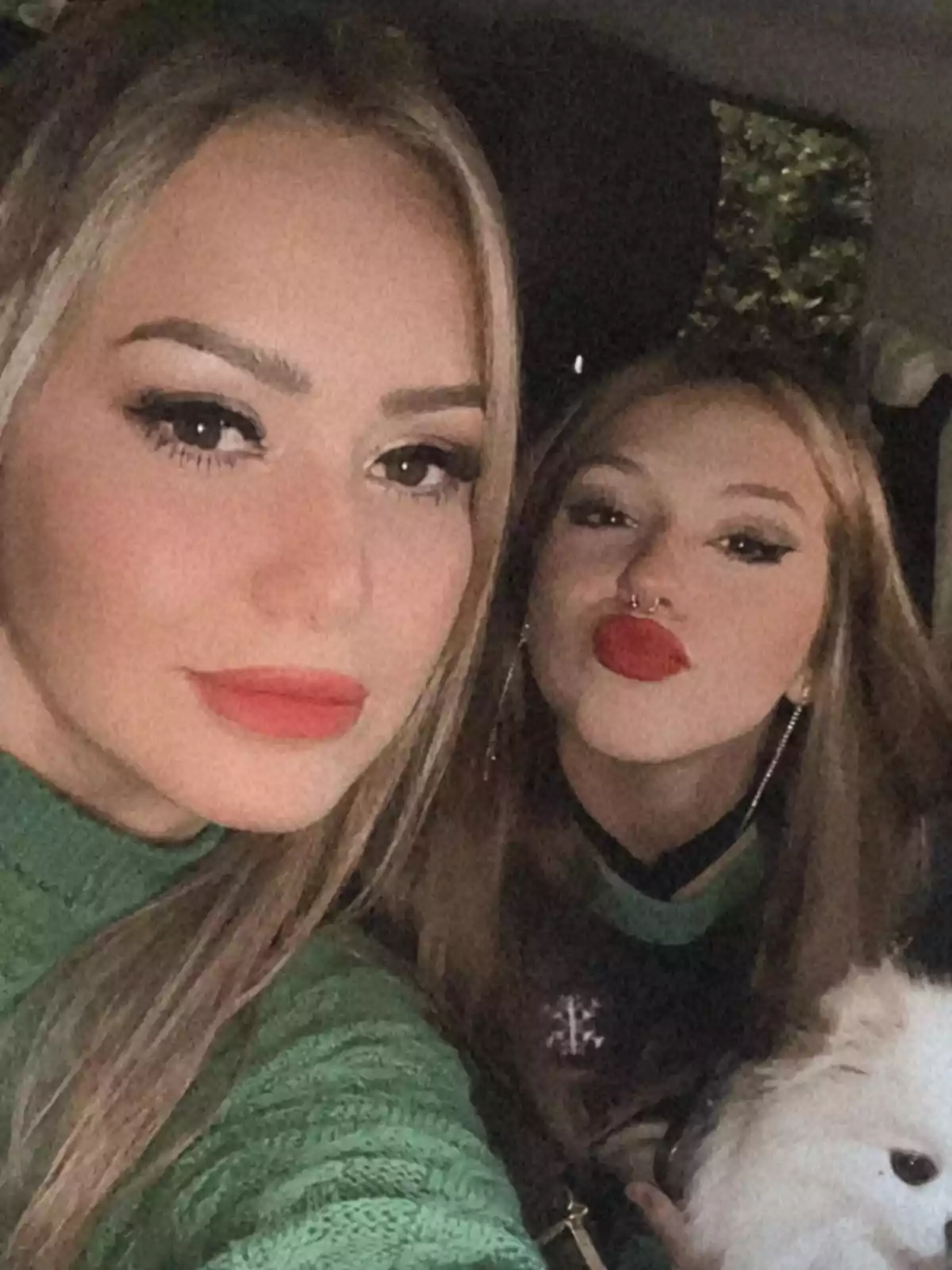 Two women in green sweaters pose for a selfie inside a car, one of them making a kissing gesture, and there is a white dog in the foreground. Two women in green sweaters pose for a selfie inside a car, one of them making a kissing gesture, and there is a white dog in the foreground.