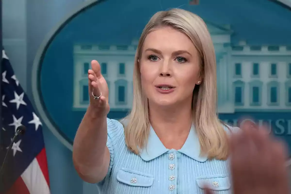 Mujer rubia hablando y gesticulando durante una conferencia de prensa con una bandera de Estados Unidos y el fondo de la Casa Blanca Mujer rubia hablando y gesticulando durante una conferencia de prensa con una bandera de Estados Unidos y el fondo de la Casa Blanca