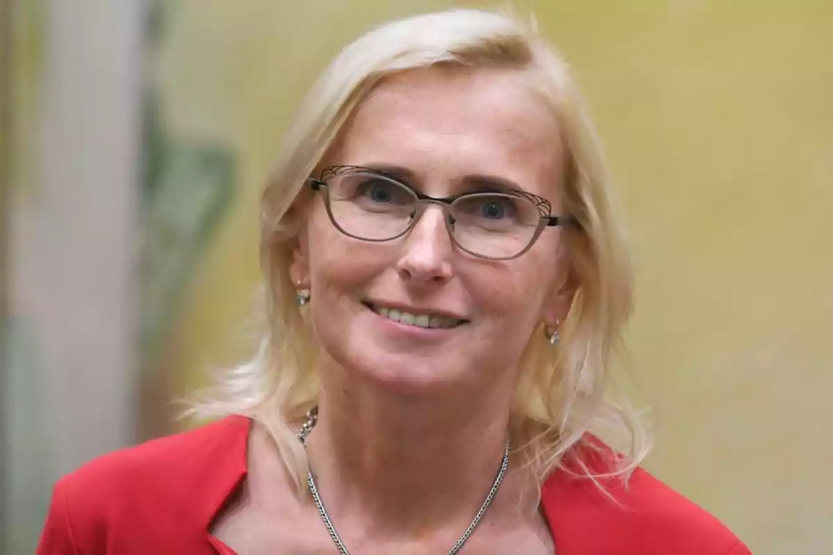 Blonde woman with glasses and a smile, wearing a red blazer and a blurred yellow background Blonde woman with glasses and a smile, wearing a red blazer and a blurred yellow background