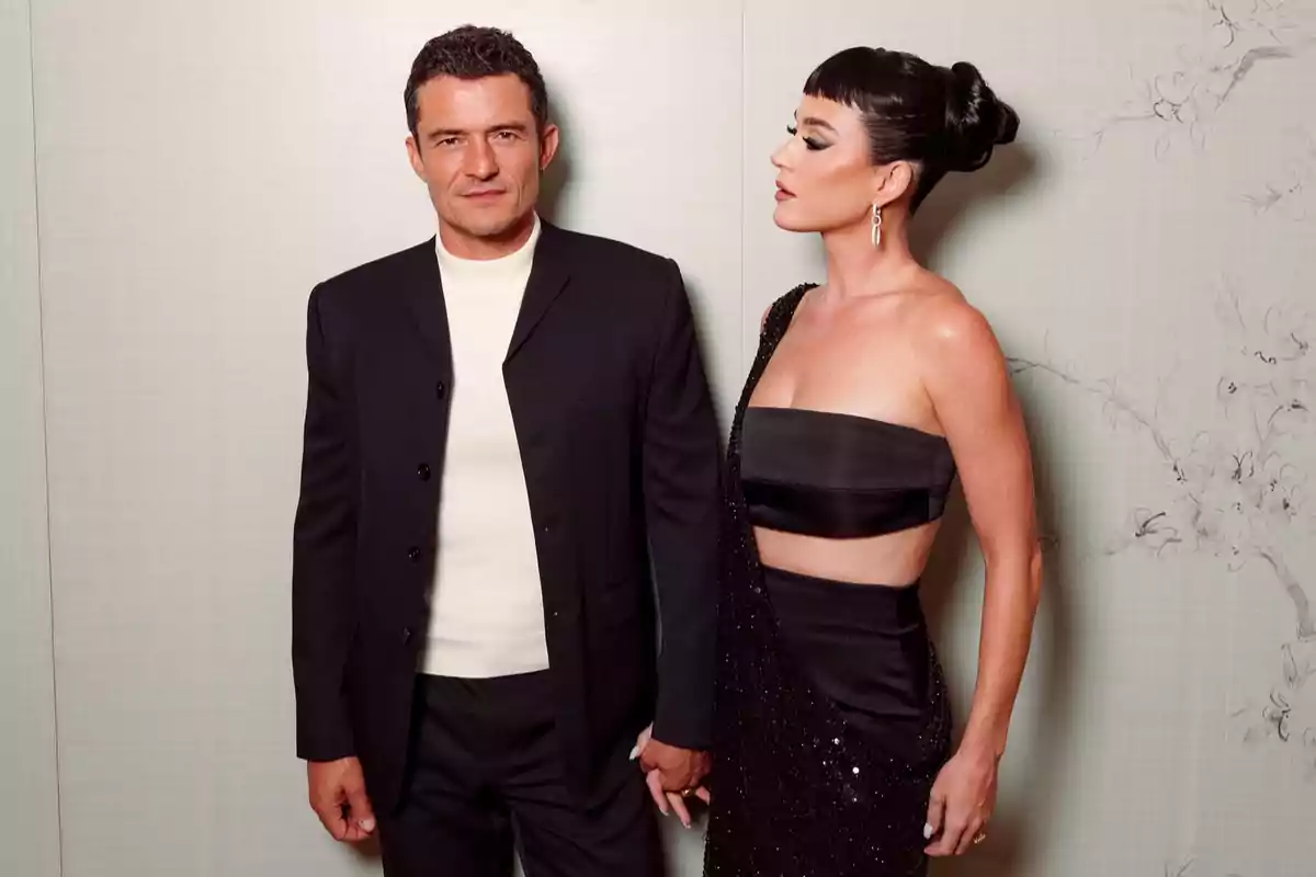 Elegant couple posing together, he in a dark suit and light sweater, she in an asymmetrical black dress and an updo hairstyle