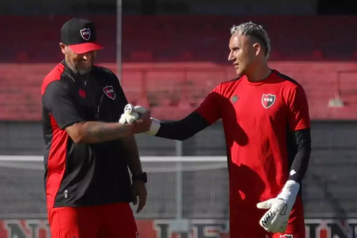 Two people wearing Newell's Old Boys sportswear greet each other on a soccer field. Two people wearing Newell's Old Boys sportswear greet each other on a soccer field.
