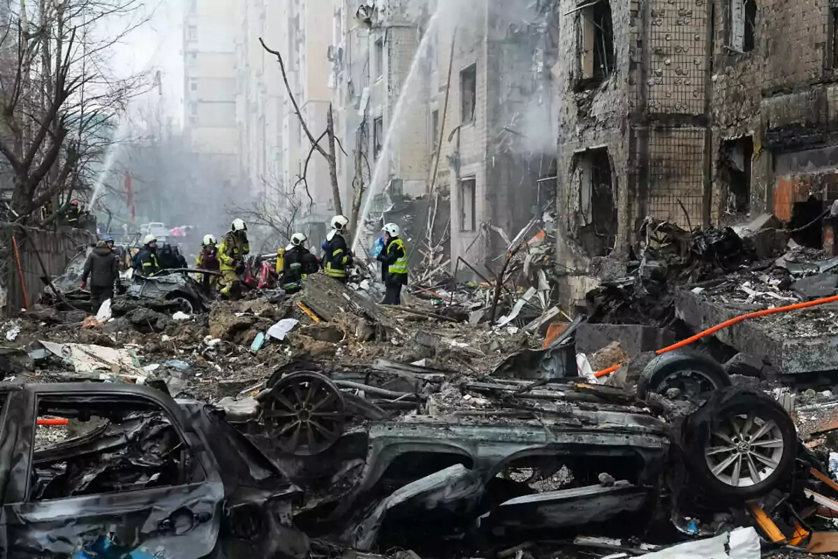 Firefighters work among the rubble of a destroyed building and charred cars after an attack in an urban area.