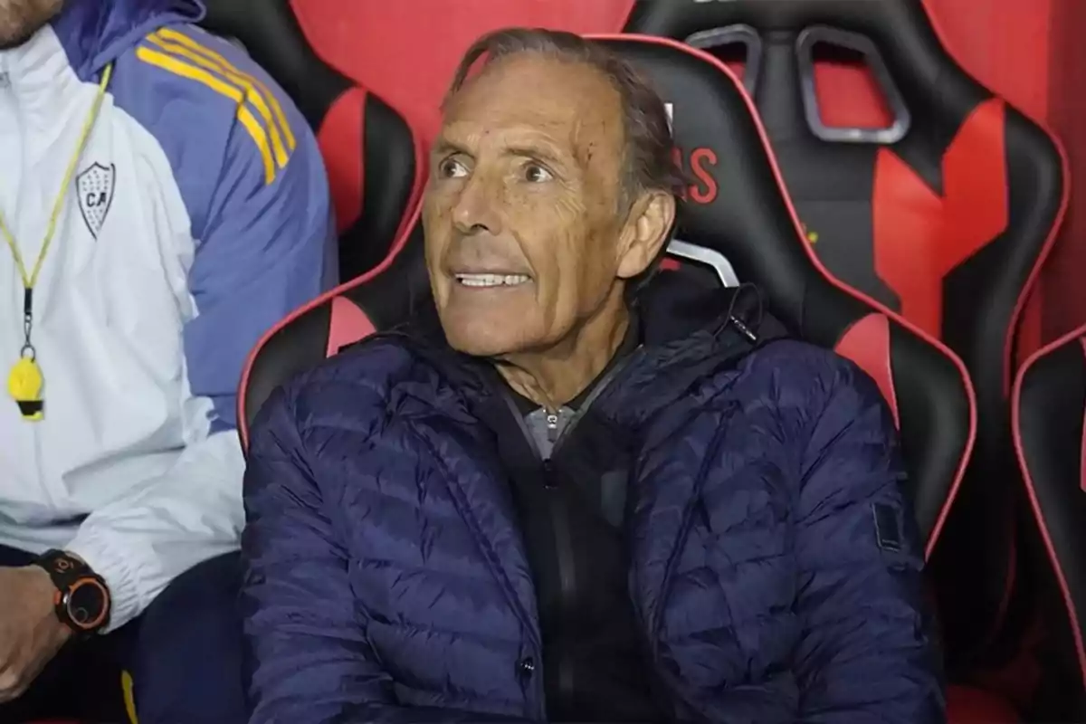 Older man in a blue jacket sitting on a sports bench looking to the side
