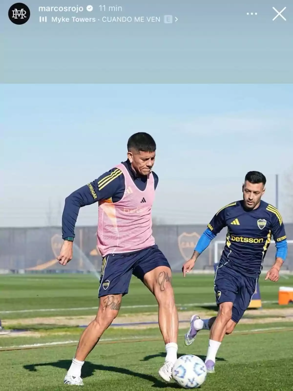 Dos futbolistas de Boca Juniors entrenan en una cancha de césped mientras compiten por el balón bajo un cielo despejado Dos futbolistas de Boca Juniors entrenan en una cancha de césped mientras compiten por el balón bajo un cielo despejado