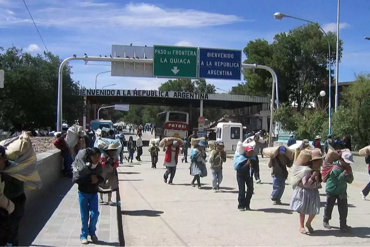 Personas cruzando la frontera entre Bolivia y Argentina cargando bultos sobre sus espaldas bajo un cielo despejado