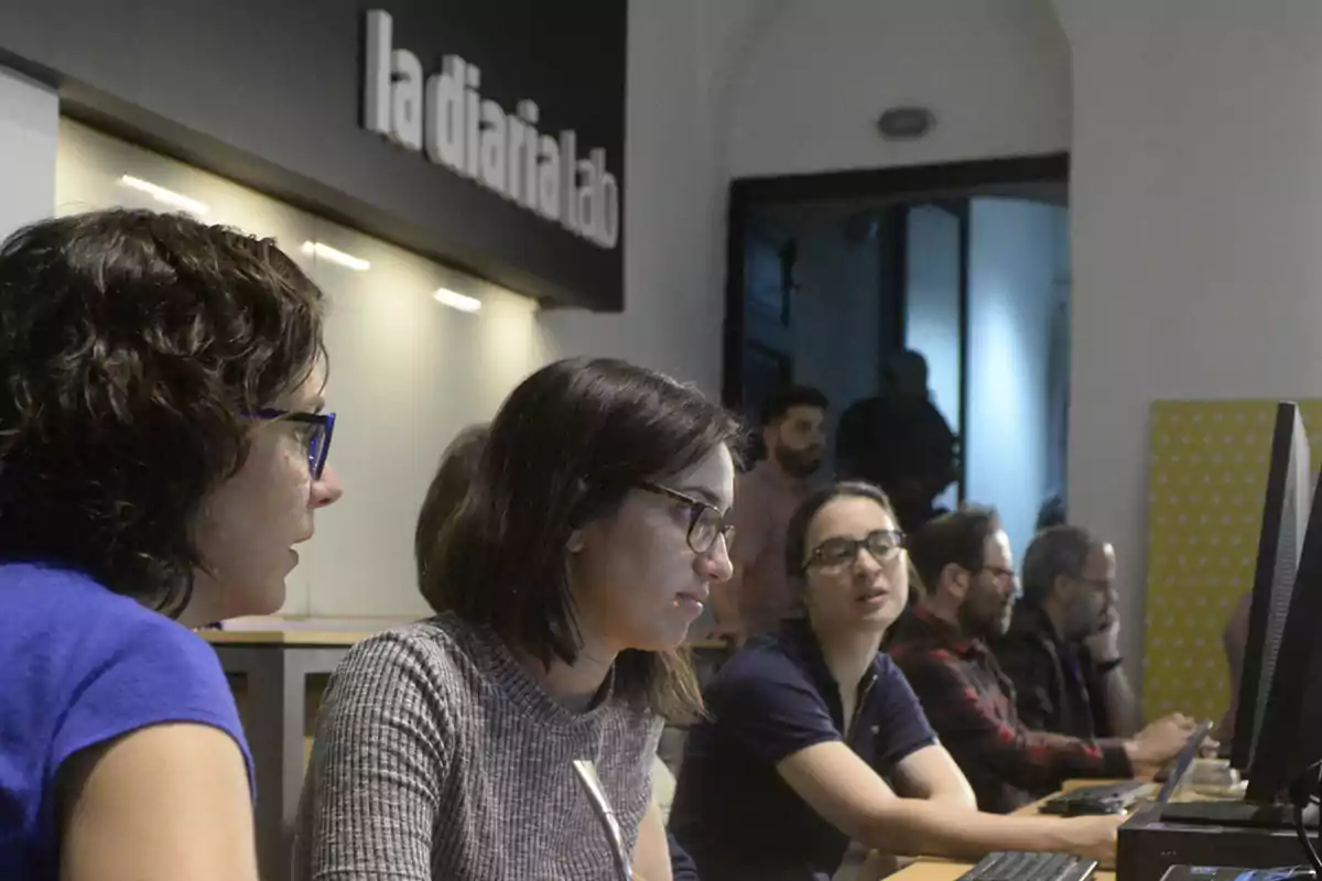 Several people are working on computers in a modern office with a sign that says Several people are working on computers in a modern office with a sign that says