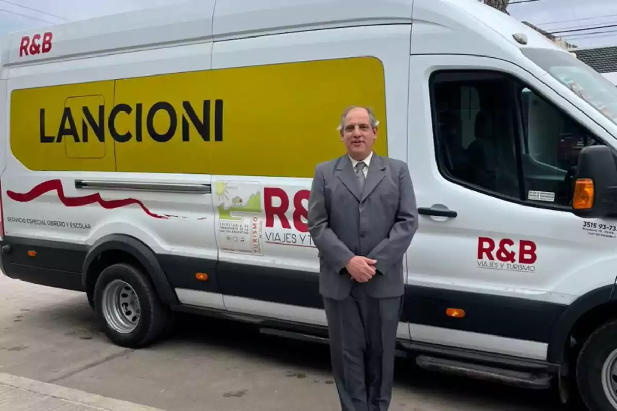 Hombre de traje gris posando frente a una camioneta blanca de transporte turístico con el logo Lancioni y R&B en el costado