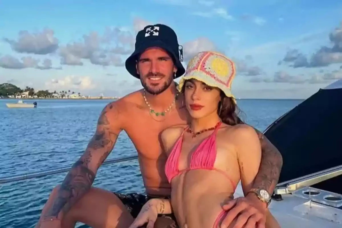 Young couple posing on a yacht over the sea on a sunny day, both wearing hats and swimsuits