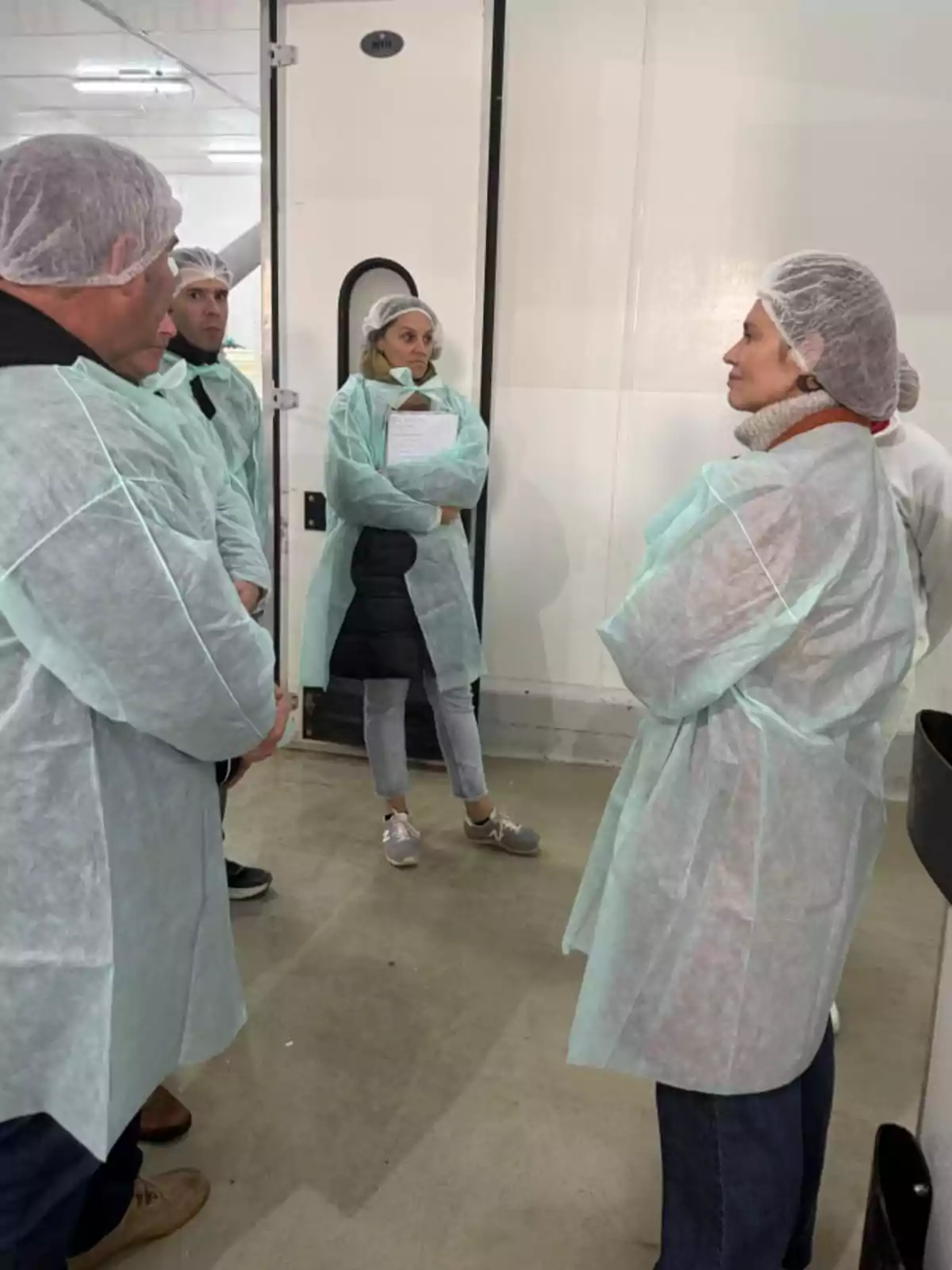 Varias personas con batas y gorros desechables conversan en el interior de una instalación industrial limpia Varias personas con batas y gorros desechables conversan en el interior de una instalación industrial limpia