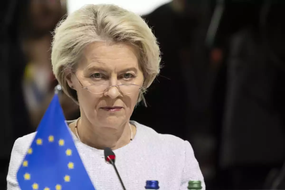 Short-haired blonde woman with glasses sitting in front of a microphone and a European Union flag Short-haired blonde woman with glasses sitting in front of a microphone and a European Union flag