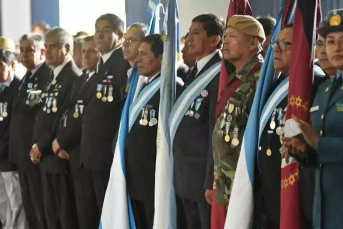 Group of veterans with medals and sashes, standing at a ceremony next to Argentine flags