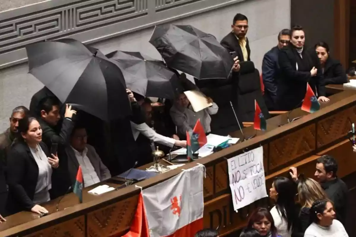 People inside a legislative chamber hold black umbrellas while others watch, and a banner with the message People inside a legislative chamber hold black umbrellas while others watch, and a banner with the message
