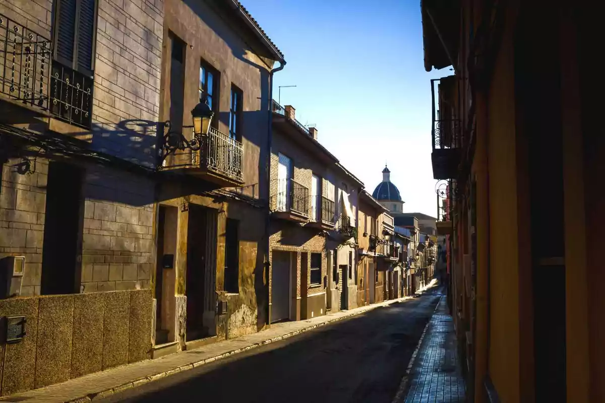 Calle estrecha de un pueblo con casas antiguas y una cúpula azul al fondo bajo la luz del atardecer Calle estrecha de un pueblo con casas antiguas y una cúpula azul al fondo bajo la luz del atardecer
