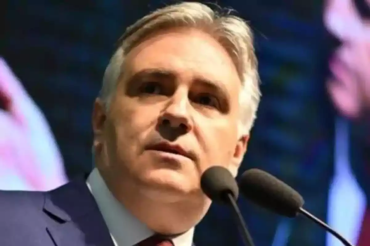 Gray-haired man speaking in front of two microphones with a dark background Gray-haired man speaking in front of two microphones with a dark background
