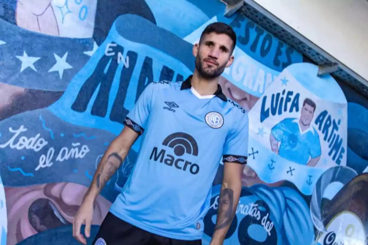 Soccer player wearing Belgrano’s light blue jersey posing in front of a mural painted with club motifs and the legend Luifa Artime. Soccer player wearing Belgrano’s light blue jersey posing in front of a mural painted with club motifs and the legend Luifa Artime.