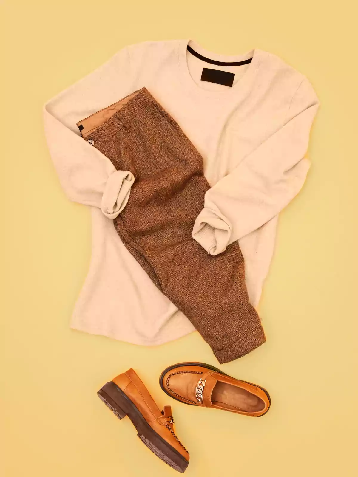 Men’s outfit consisting of a beige sweater, brown pants, and brown loafers on a yellow background Men’s outfit consisting of a beige sweater, brown pants, and brown loafers on a yellow background