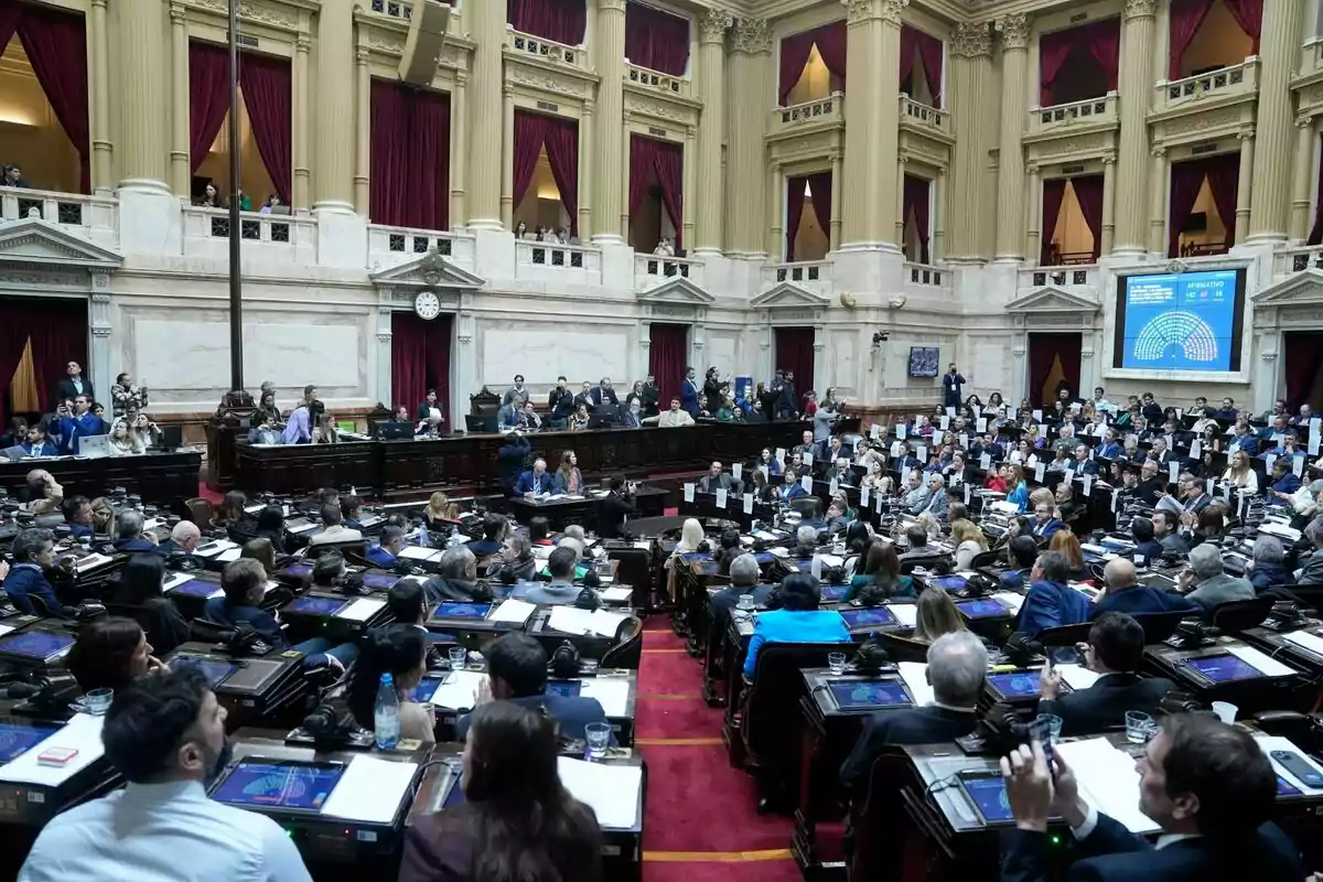 Parliamentary session in a chamber with numerous legislators seated at their desks and a large screen displaying voting results Parliamentary session in a chamber with numerous legislators seated at their desks and a large screen displaying voting results