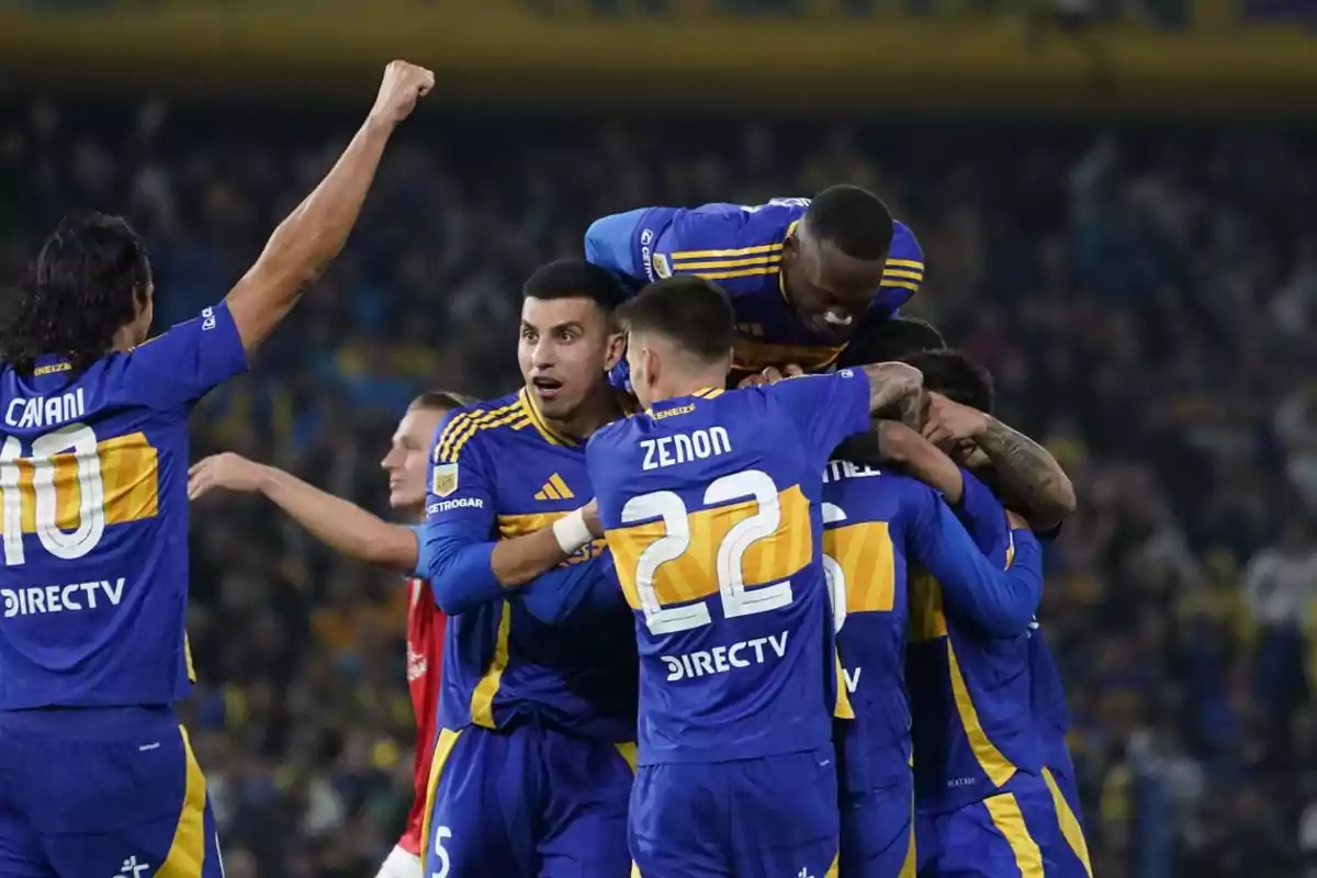 Players from a soccer team wearing blue and yellow uniforms celebrate a goal by hugging on the field in front of a crowd. Players from a soccer team wearing blue and yellow uniforms celebrate a goal by hugging on the field in front of a crowd.