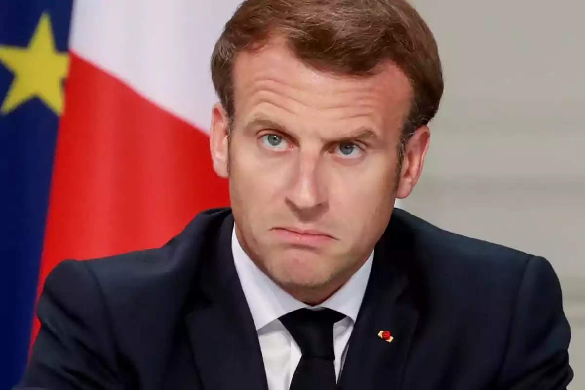 Man in a dark suit with a serious expression in front of a tricolor flag Man in a dark suit with a serious expression in front of a tricolor flag