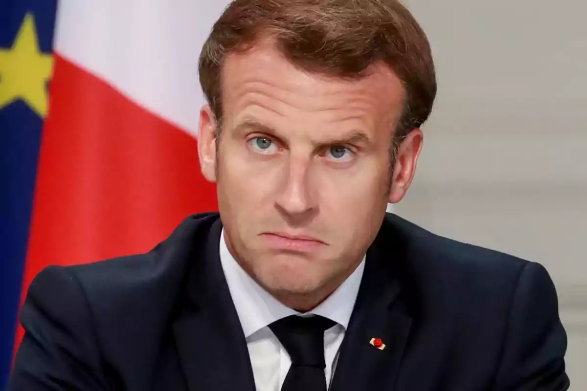 Man in a dark suit with a serious expression and flags in the background