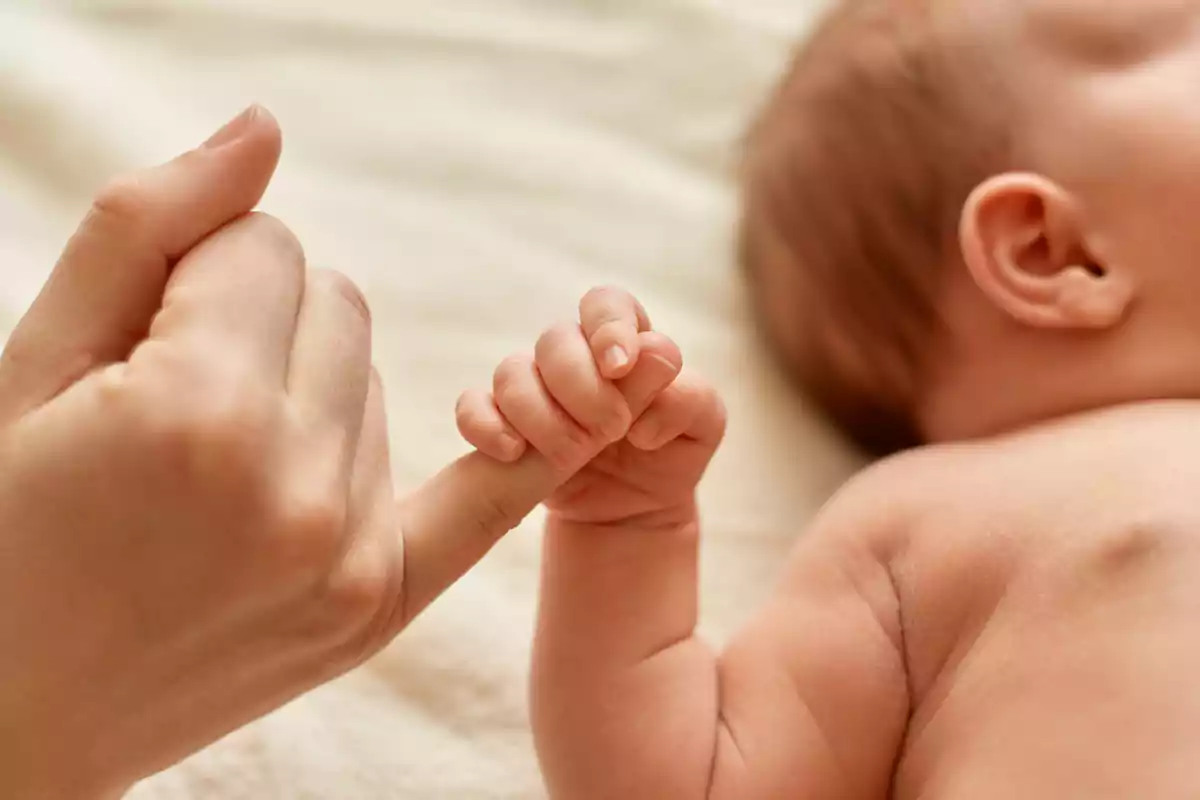 Mano de un bebé sujetando el dedo de un adulto sobre una manta clara