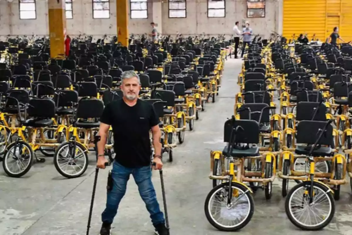 Man standing with crutches in a warehouse full of tricycles adapted for people with disabilities