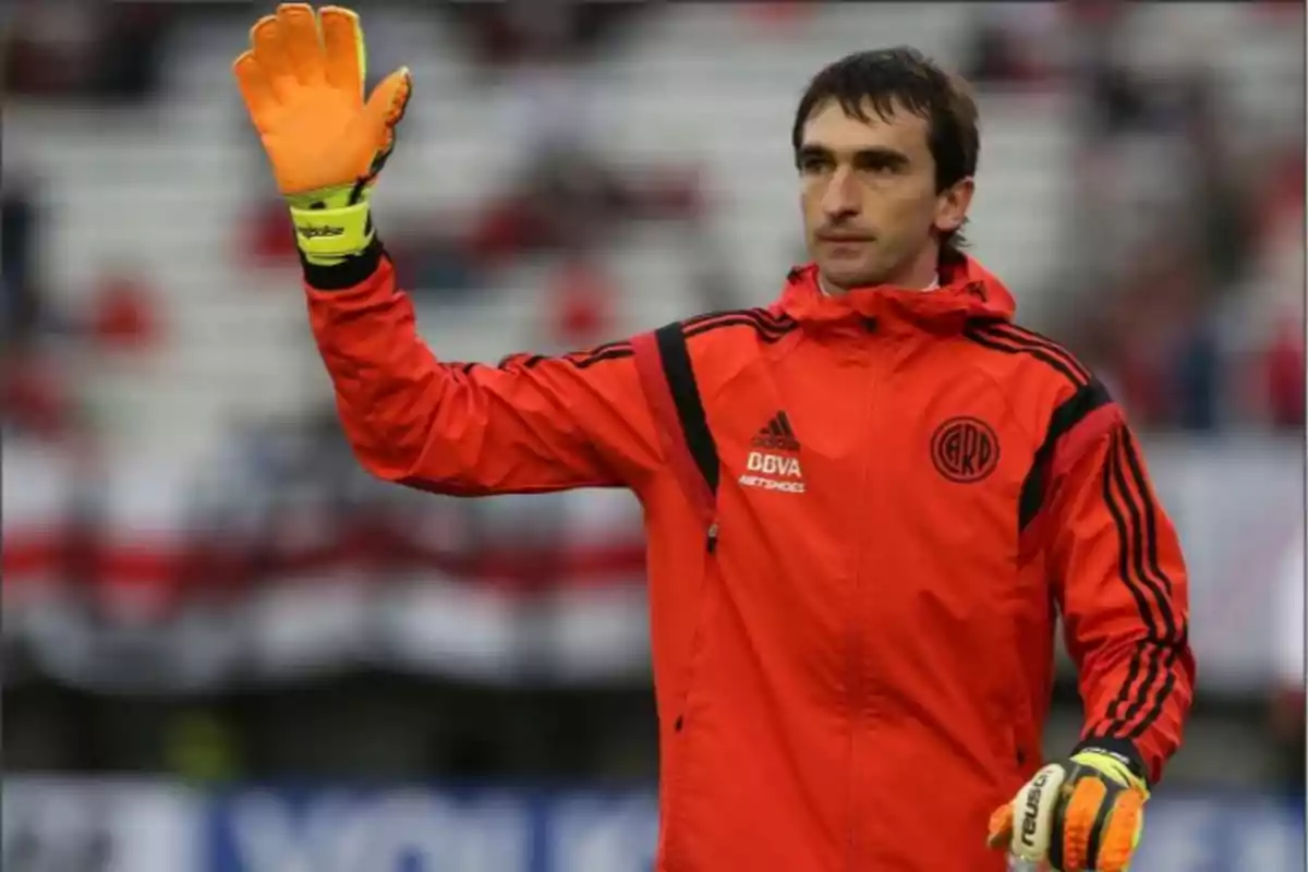 Portero de fútbol con guantes naranjas y chaqueta roja de River Plate saludando en un estadio Portero de fútbol con guantes naranjas y chaqueta roja de River Plate saludando en un estadio
