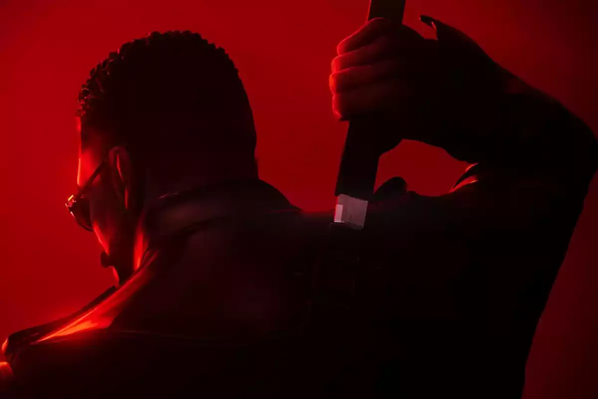 Hombre de espaldas con gafas oscuras y chaqueta de cuero sosteniendo una espada sobre un fondo rojo intenso Hombre de espaldas con gafas oscuras y chaqueta de cuero sosteniendo una espada sobre un fondo rojo intenso