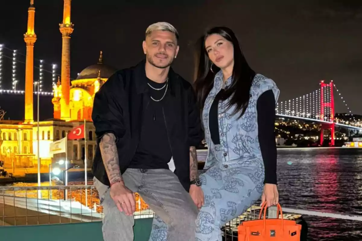 Una pareja posa junto a un río de noche con una mezquita iluminada y un puente con luces al fondo Una pareja posa junto a un río de noche con una mezquita iluminada y un puente con luces al fondo