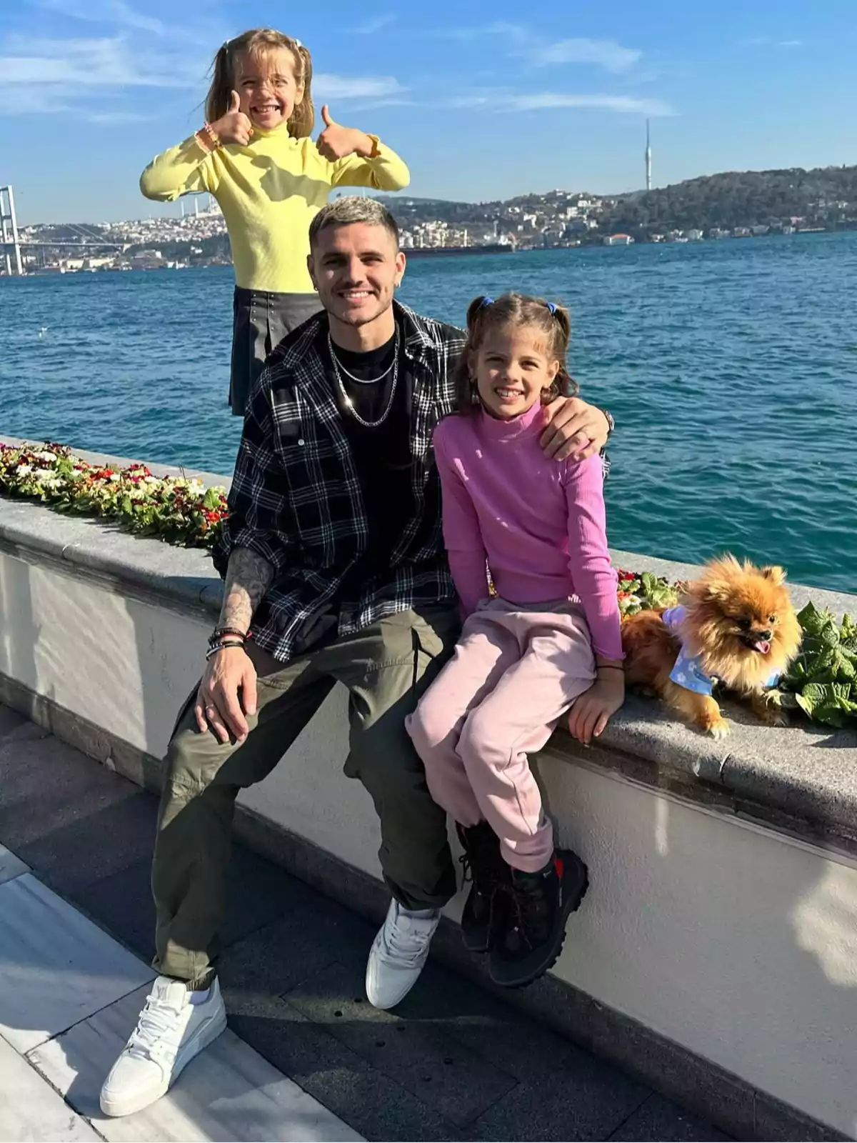 A man and two girls smile with a small dog in front of a seaside cityscape on a sunny day. A man and two girls smile with a small dog in front of a seaside cityscape on a sunny day.