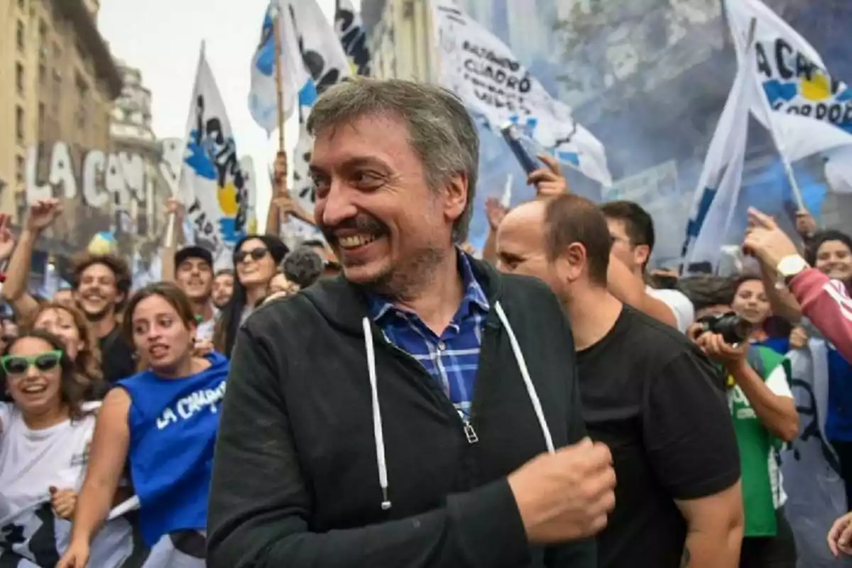 Hombre sonriente en primer plano rodeado de una multitud en una manifestación con banderas y ambiente festivo Hombre sonriente en primer plano rodeado de una multitud en una manifestación con banderas y ambiente festivo