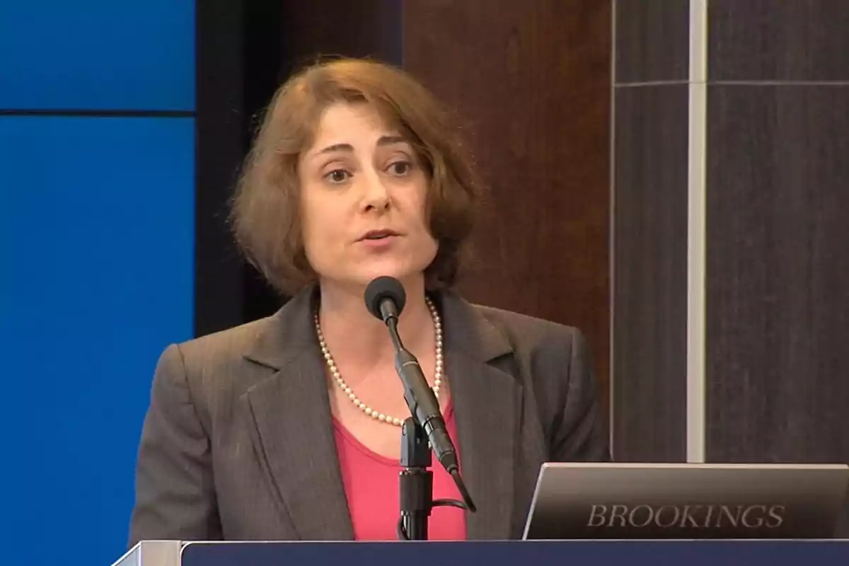 Short-haired brunette woman speaking into a microphone at a podium with the word Brookings. Short-haired brunette woman speaking into a microphone at a podium with the word Brookings.