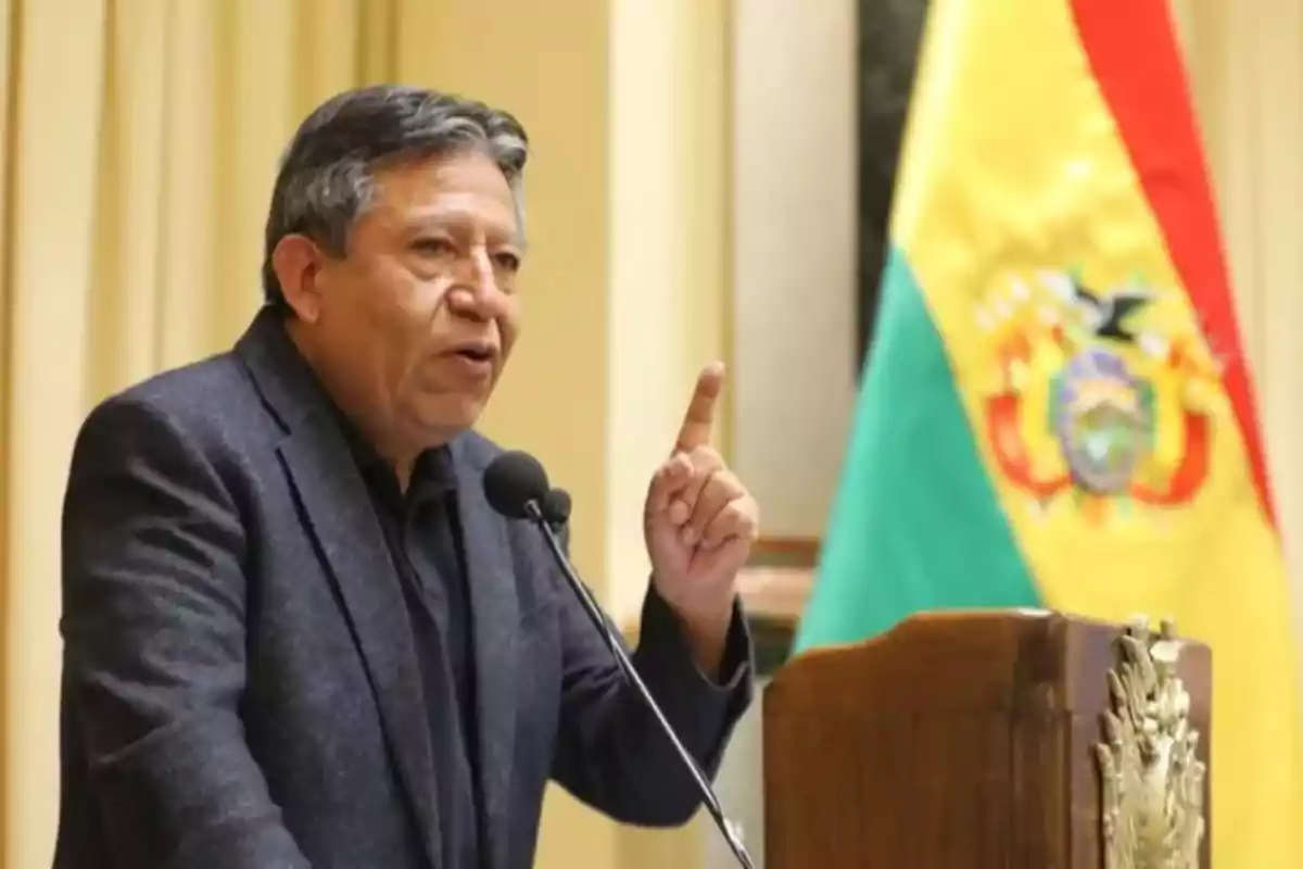 Man speaking at a podium with a microphone and the Bolivian flag in the background