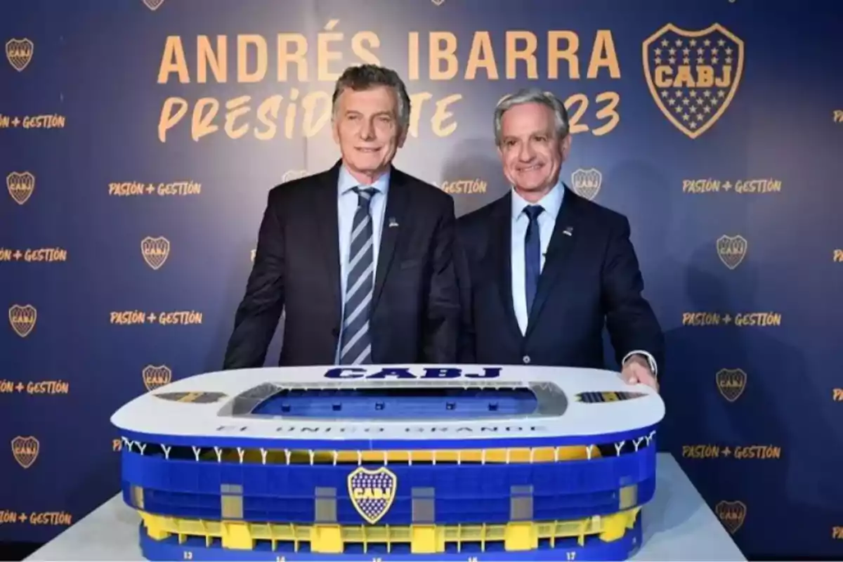 Dos hombres de traje posan sonrientes detrás de una maqueta del estadio de Boca Juniors con un fondo azul que tiene el escudo del club y el nombre Andrés Ibarra presidente 2023 Dos hombres de traje posan sonrientes detrás de una maqueta del estadio de Boca Juniors con un fondo azul que tiene el escudo del club y el nombre Andrés Ibarra presidente 2023
