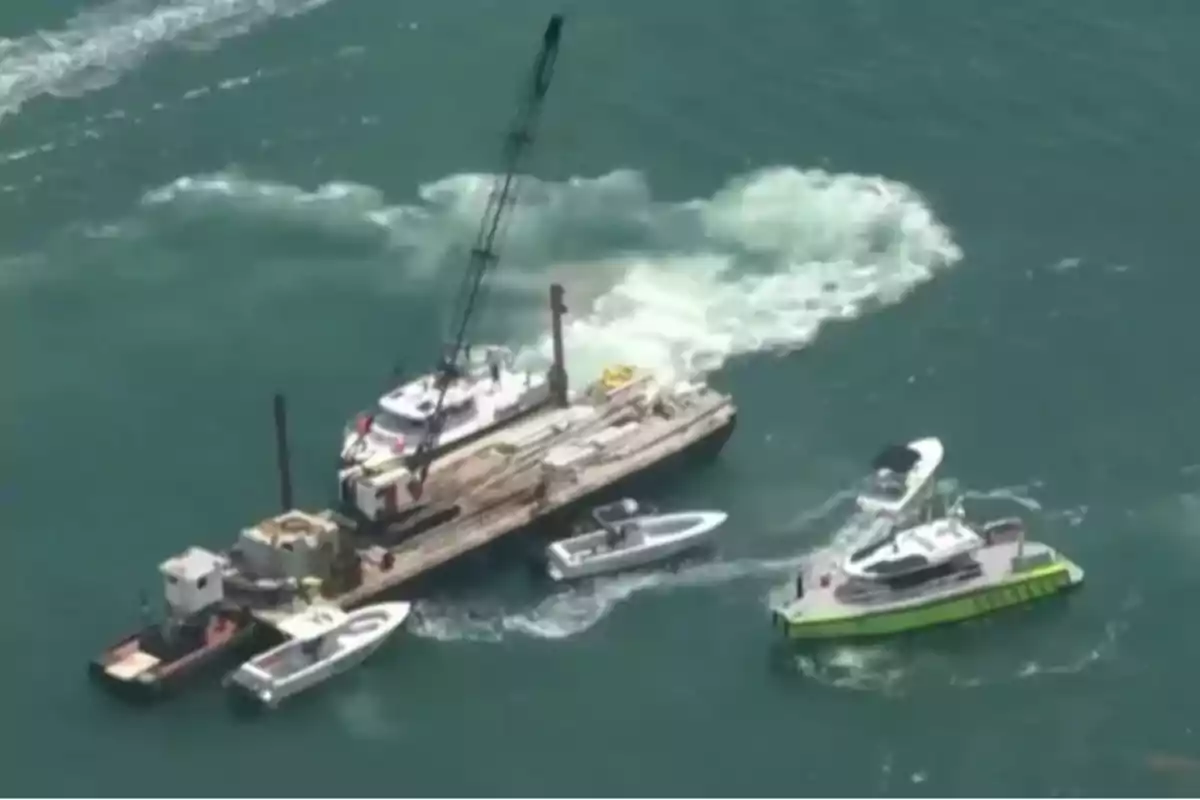 Varias embarcaciones rodean una barcaza con grúa en el mar, mientras se observa una gran turbulencia en el agua cercana.