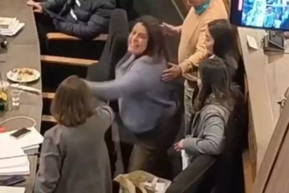 Angry woman tries to hit another person in a meeting room while several people watch and one tries to stop her. Angry woman tries to hit another person in a meeting room while several people watch and one tries to stop her.