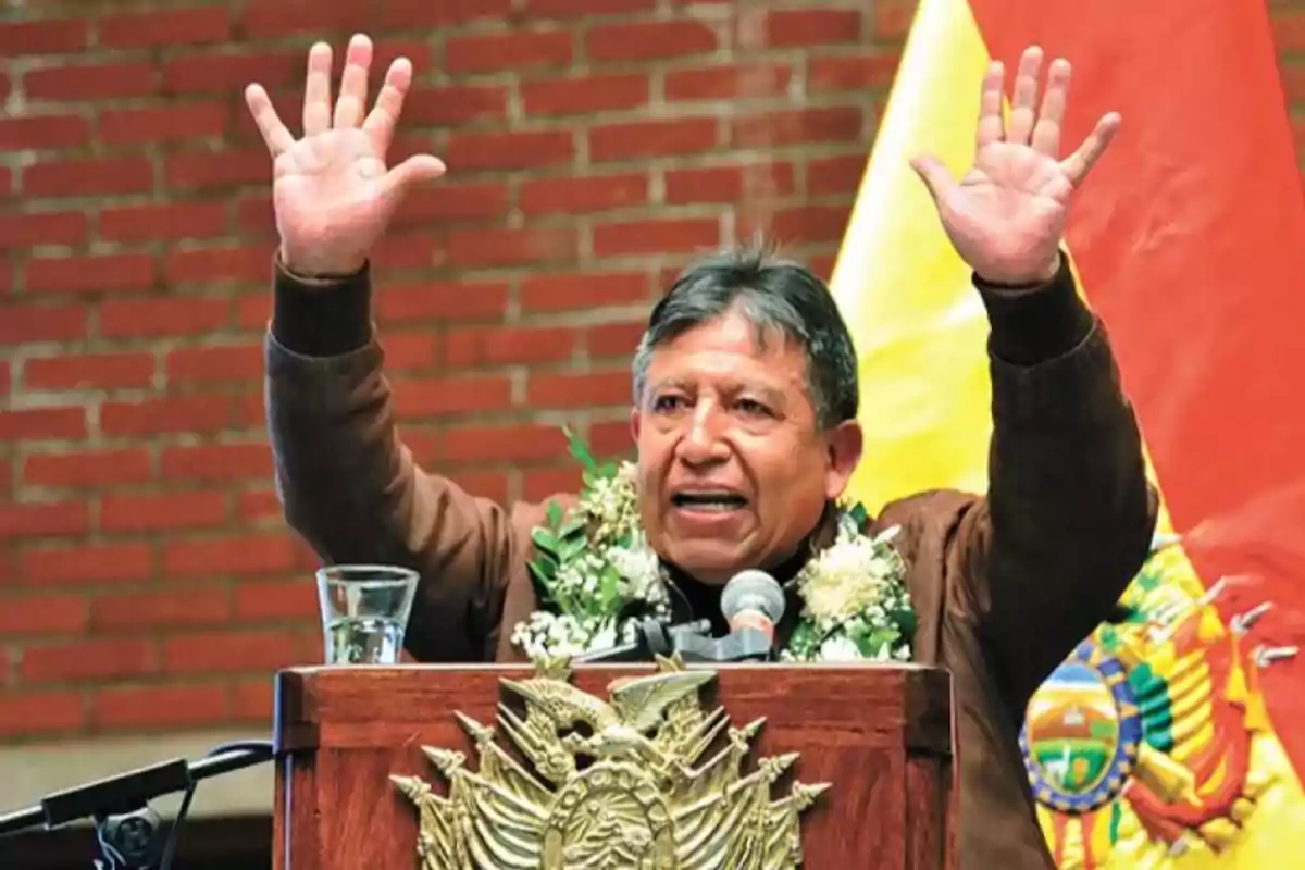 Hombre hablando en un podio con las manos levantadas, usando una guirnalda de flores y con una bandera de Bolivia de fondo Hombre hablando en un podio con las manos levantadas, usando una guirnalda de flores y con una bandera de Bolivia de fondo