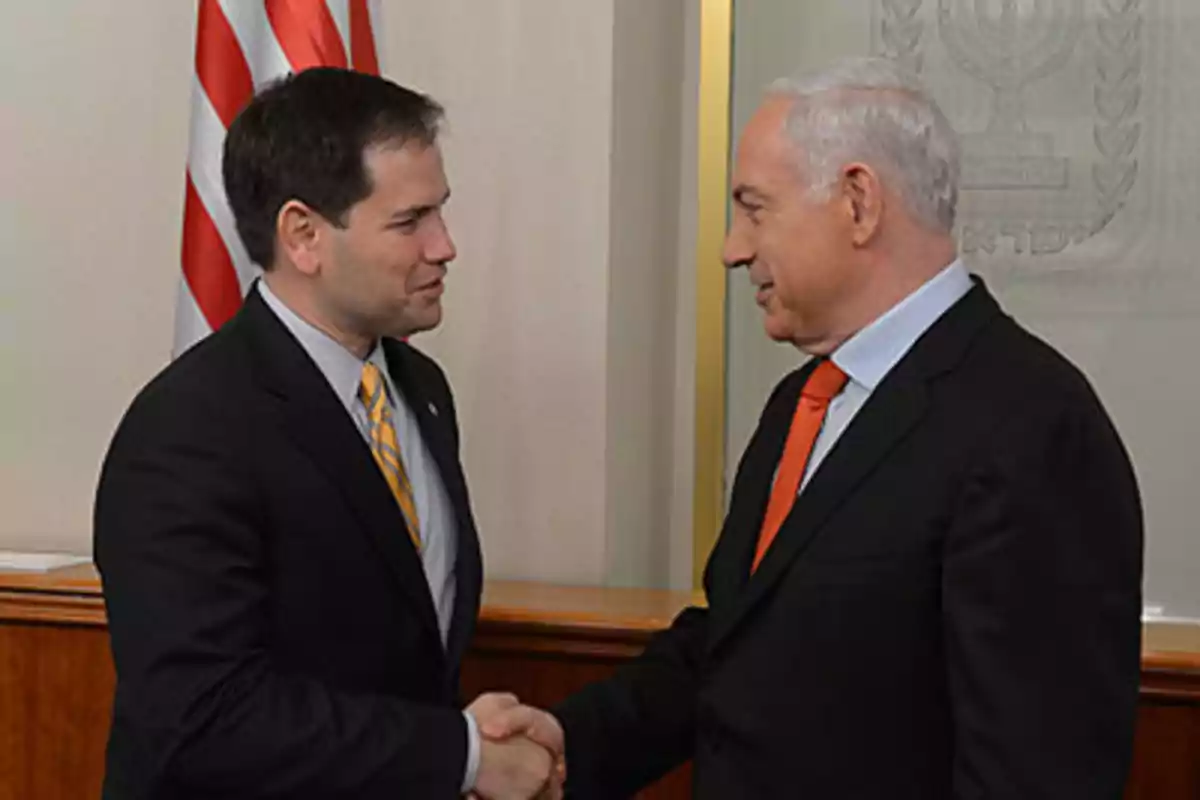 Two men in suits shake hands and smile at each other in a formal setting with a flag in the background. Two men in suits shake hands and smile at each other in a formal setting with a flag in the background.