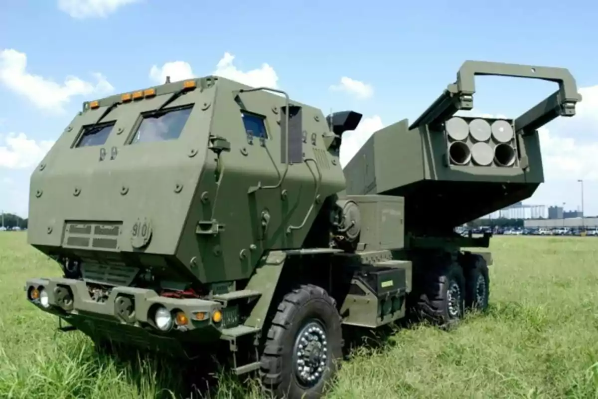 Green military vehicle equipped with a multiple rocket launcher system parked on grass under a clear sky