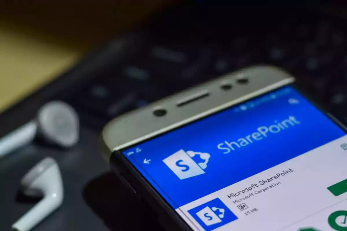 Mobile phone displaying the Microsoft SharePoint app on screen with white headphones next to it on a black keyboard. Mobile phone displaying the Microsoft SharePoint app on screen with white headphones next to it on a black keyboard.