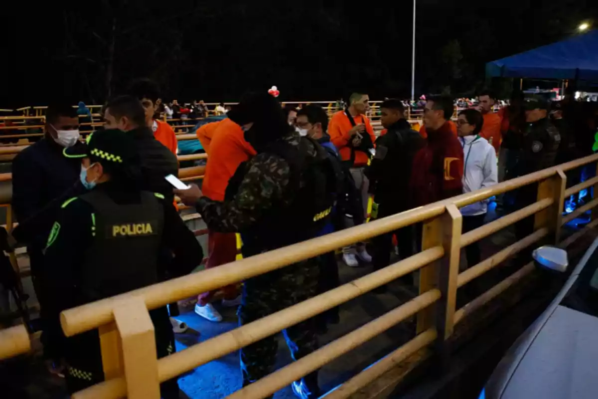 A group of people lines up on a bridge while police officers and security personnel check documents in a nighttime setting. A group of people lines up on a bridge while police officers and security personnel check documents in a nighttime setting.