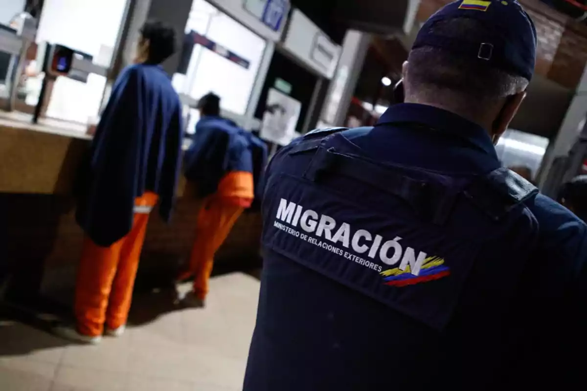 Immigration officer in a blue uniform supervises people at a control window in a station or border post